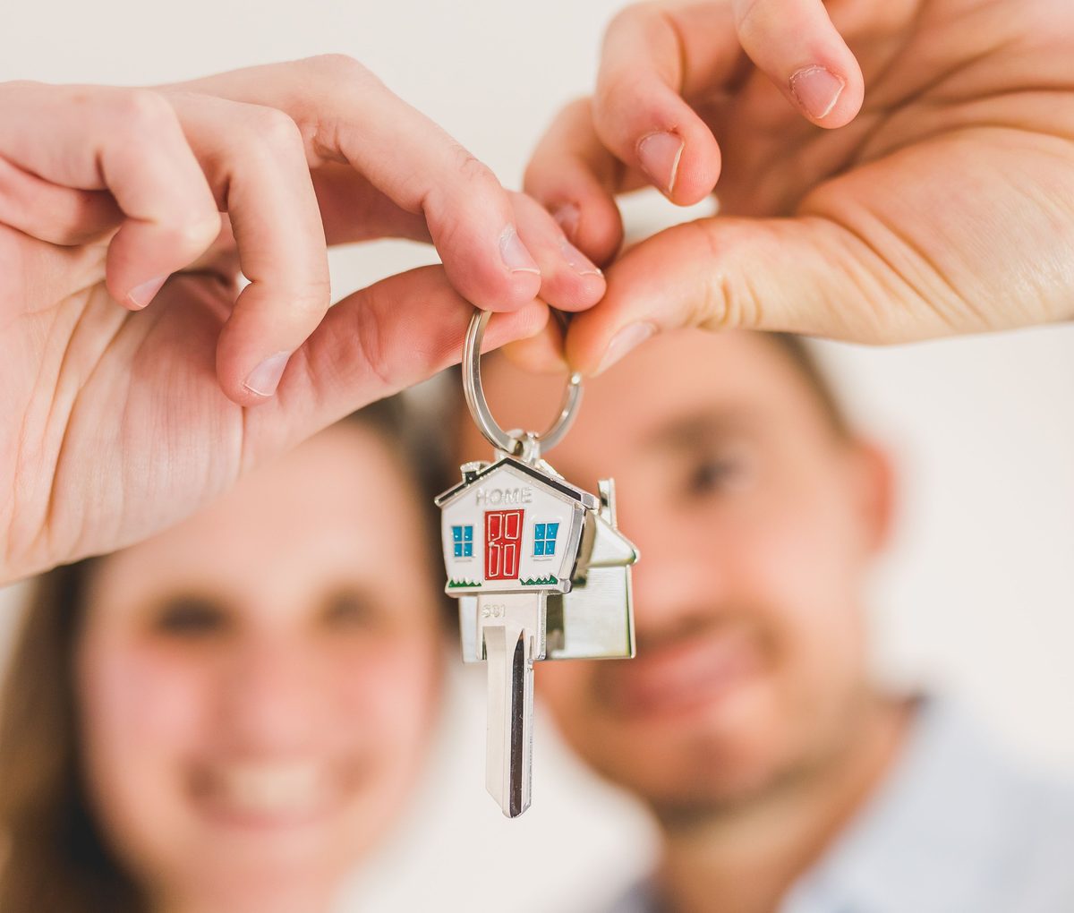 A couple holding up a house-shaped keyring, smiling out of focus behind it